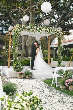 a bride and groom are standing under an arch with flowers on the ground in front of them