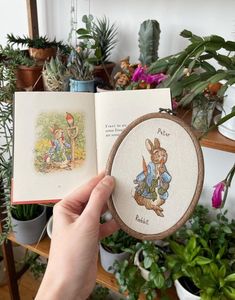 a person holding an open book in front of some potted plants and other items