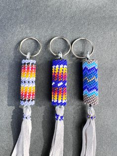 three keychains with different colors and designs on them, one has a tassel