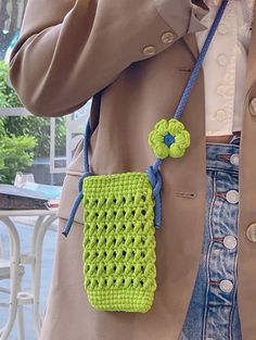 a woman wearing a trench coat and holding a cell phone up to her ear with a crocheted purse on it