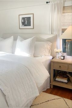 a bed with white linens and pillows in a bedroom next to a lamp on a table