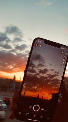 a person holding up a cell phone in front of a sunset with cars on the road