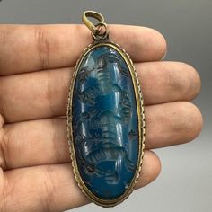 a hand holding a pendant with a blue stone in the shape of an elephant on it's side