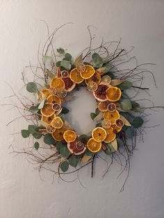 a wreath made out of dried oranges and leaves on a white wall with greenery