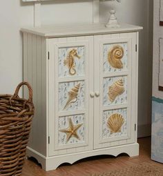 a white cabinet with gold seahorses and shells painted on the doors is next to a wicker basket