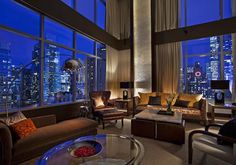 a living room filled with lots of furniture and tall buildings in the background at night