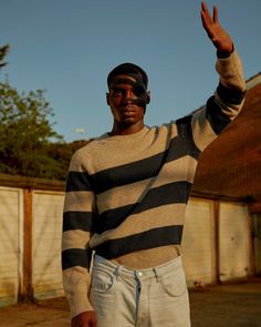 a man in striped sweater and white pants waving at the camera with his hand up