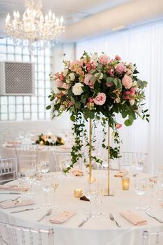 a tall vase filled with pink and white flowers on top of a table covered in silverware