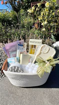 a white basket filled with lots of items on top of a cement ground next to flowers