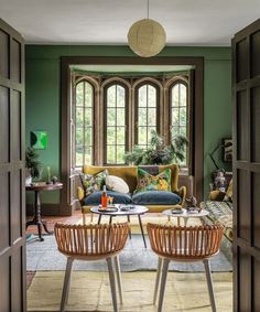 two wicker chairs sit in front of a green living room with arched doors and windows