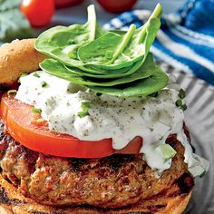 a burger with tomatoes, lettuce and sour cream on top is sitting on a plate