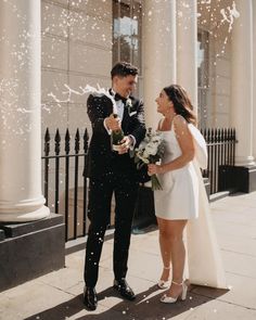 a bride and groom are standing outside in front of the columns with confetti