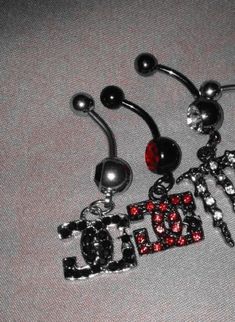 three different types of belly piercings with red and black crystals on them, one is for the word love