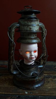 a creepy doll with glowing eyes sitting in a caged container on top of a wooden table