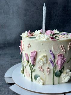 a white cake decorated with flowers and a single candle