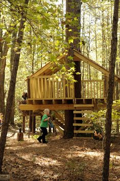 a tree house in the woods surrounded by trees and people walking around it with children