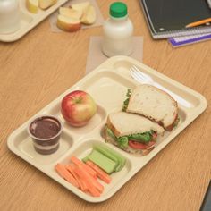 a lunch tray with an apple, carrots and sandwich