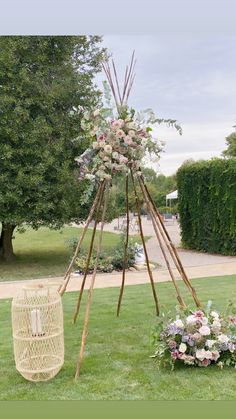 a teepee is set up in the grass with flowers and greenery around it