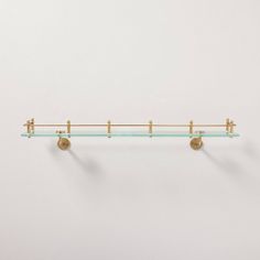 a glass shelf with three brass hooks on it