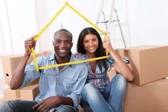 a man and woman sitting on cardboard boxes holding up a yellow frame