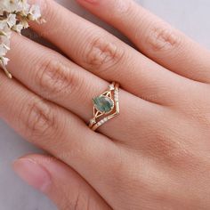 a woman's hand wearing a gold ring with a green stone and diamond accents