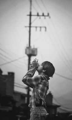 black and white photograph of a young boy drinking from a bottle in front of power lines