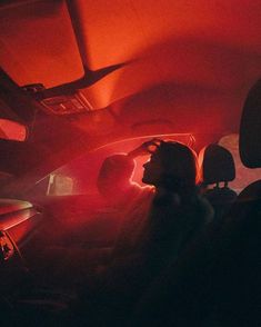 two people sitting in the back seat of a car with red light coming from behind them