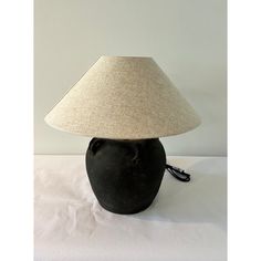 a black vase with a lamp on top of it sitting on a white tablecloth