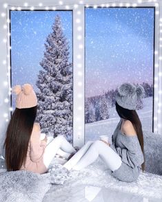 two young women sitting on a bed looking out the window at snow covered trees outside