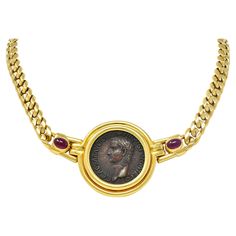 Comprised of curb link chain centering an ancient coin bezel set in hinged station Measuring 25.0 mm round - deep matte brownish bronze with antique patina Depicting a cameo bust of the ancient Roman emperor Caligula in profile Reverse depicts the Roman goddess of fertility, Vesta seated on throne Bezel is fluted and inscribed on back 'ROMA CALIGULA 37-41 ASSE' Flanked by hinged shoulders featuring bezel set ruby cabochons Oval shaped and weighing approximately 2.80 carats total Transparent medi Luxury Bronze Necklace For Formal Occasions, Luxury Bronze Necklaces For Formal Occasions, Antique Coin Pendant Necklace For Formal Occasions, Antique Gold Coin-shaped Jewelry With Antique Finish, Elegant Coin Necklace For Formal Occasions, Gold Vintage Jewelry For Formal Occasions, Bronze Byzantine Round Jewelry, Antique Finish Yellow Gold Round Jewelry, Luxury Antique Finish Jewelry For Formal Occasions