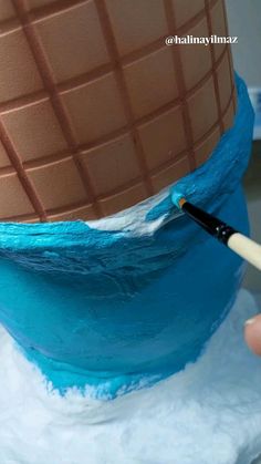 someone is painting the side of a cake with blue icing and white frosting