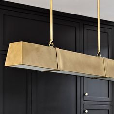 a large rectangular light fixture hanging from the ceiling in a black and gold colored kitchen