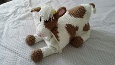 a crocheted cow laying on top of a white bed covered in blankets and pillows