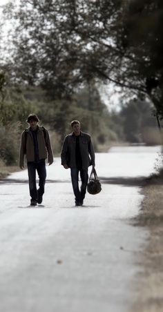 two men walking down the road with their bags in hand and one carrying a bag