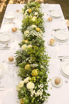 a long table with white plates and flowers on it is set for an outdoor dinner