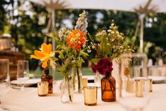 several vases filled with flowers sitting on top of a white table covered in wine glasses