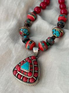 A beautiful Tibetan-Nepali style silver-plated vintage pendant with coral and turquoise exudes a unique and captivating ethnic charm. Red Bohemian Necklace With Large Pendant, Traditional Beaded Turquoise Pendant Necklace, Traditional Turquoise Necklace With Colorful Beads For Gift, Spiritual Turquoise Pendant Necklace For Festival, Traditional Turquoise Necklace For Festivals With Silver Accents, Traditional Turquoise Necklace With Natural Stones For Festivals, Red Bohemian Round Pendant Jewelry, Traditional Silver Turquoise Necklace For Festivals, Traditional Turquoise Pendant Necklace With Natural Stones