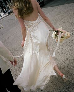 a woman in a white dress walking down the street with a bouquet on her hand