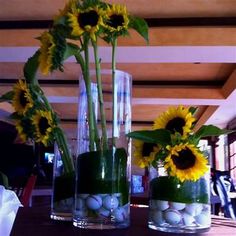 three vases with sunflowers and balls in them sitting on a wooden table