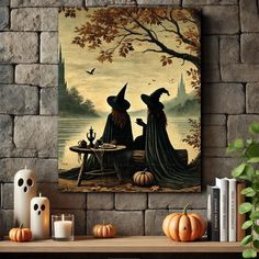 two witches sitting at a table in front of a lake with pumpkins on the ground