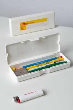 an open white box with pencils and erasers in it next to a lighter