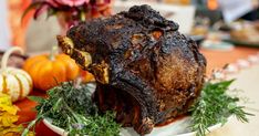 a large piece of meat sitting on top of a white plate next to flowers and pumpkins