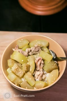 a bowl filled with food sitting on top of a wooden table next to a spoon