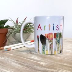 a coffee mug with the words artist on it next to pencils and potted plant