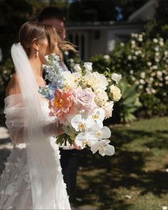 a bride holding a bouquet of white and pink flowers in front of her groom on his wedding day