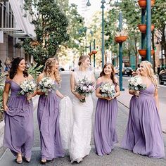 a group of women standing next to each other on a sidewalk holding bouquets in their hands