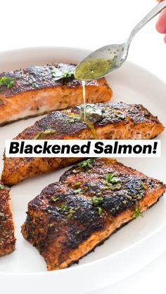 someone is dipping sauce on some salmon on a white plate with lemons and parsley