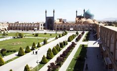 an aerial view of a large building with many trees in the foreground and people walking around