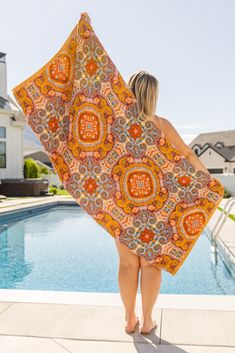 a woman is standing by the pool with an orange and yellow blanket on her back