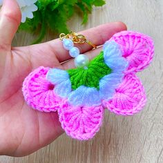 a hand holding a small crocheted flower brooch in pink, blue and green